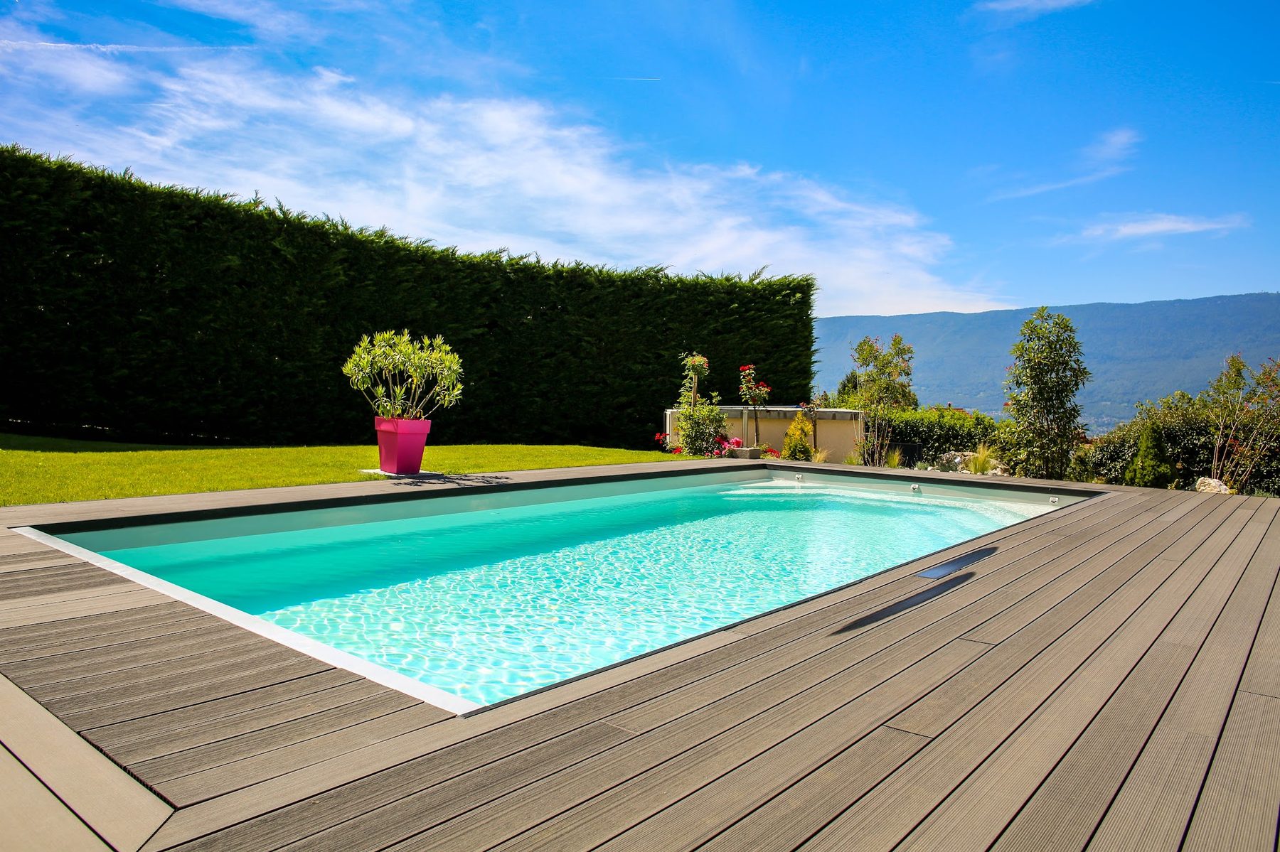Piscine rectangulaire bordée d'une terrasse en lames, pelouse et haie de cyprès